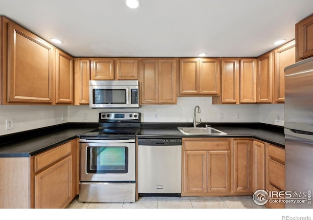 kitchen featuring light tile patterned floors, stainless steel appliances, dark countertops, recessed lighting, and a sink