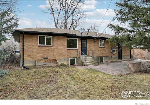 back of house featuring roof with shingles, brick siding, a lawn, a patio area, and fence