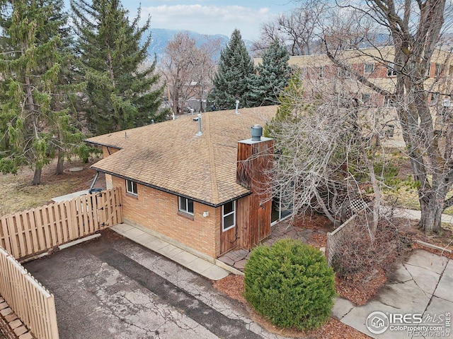 view of side of home with roof with shingles, driveway, and brick siding