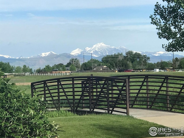 view of gate with fence, a mountain view, a lawn, and a rural view