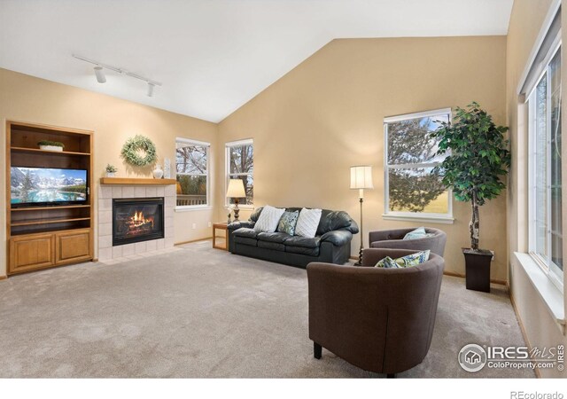 carpeted living room with plenty of natural light, track lighting, vaulted ceiling, and a tiled fireplace