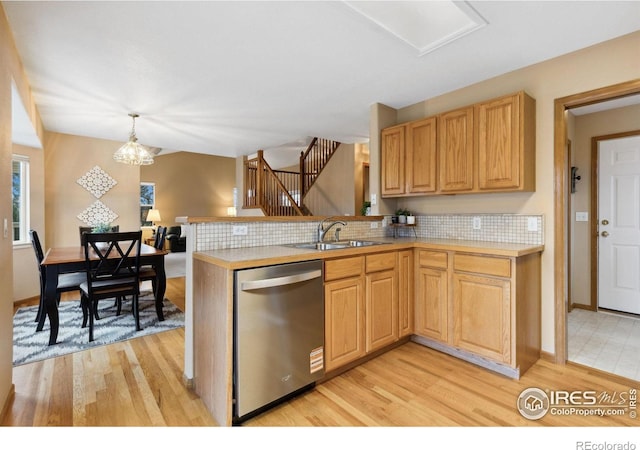 kitchen with light wood finished floors, stainless steel dishwasher, an inviting chandelier, a sink, and a peninsula