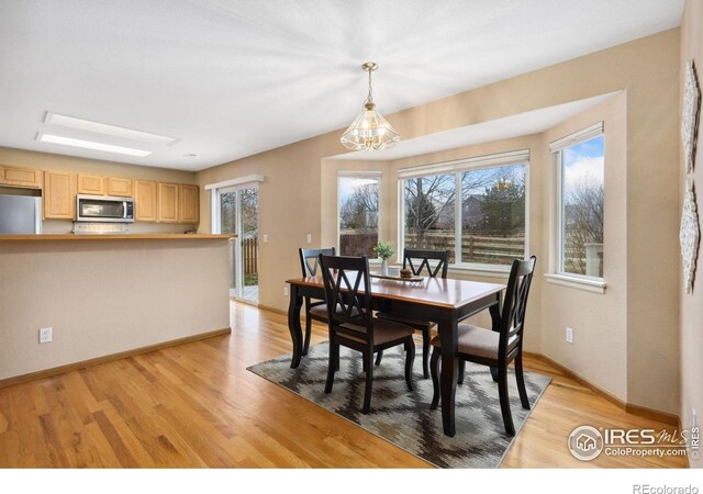 dining space featuring light wood finished floors, baseboards, and a notable chandelier