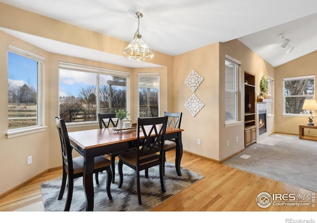 dining room with light wood finished floors, baseboards, a glass covered fireplace, lofted ceiling, and rail lighting