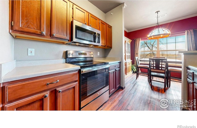 kitchen featuring crown molding, light countertops, light wood-style flooring, appliances with stainless steel finishes, and brown cabinetry