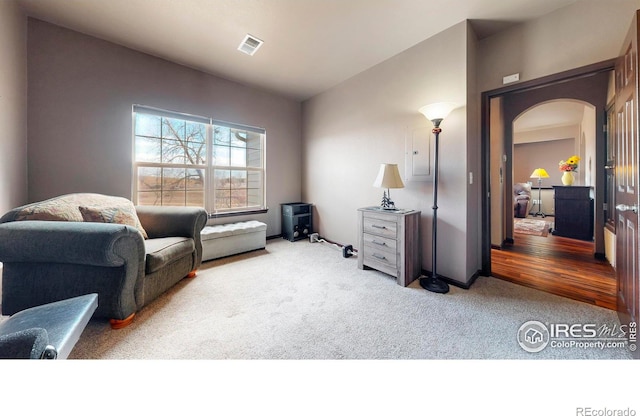 sitting room featuring carpet floors, visible vents, arched walkways, and lofted ceiling