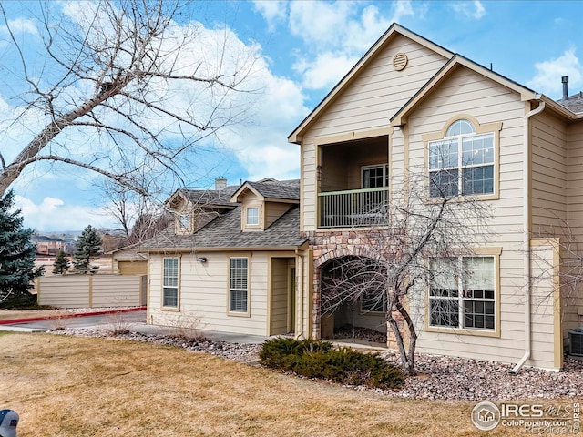 view of front of property featuring a shingled roof, cooling unit, a balcony, and a front lawn