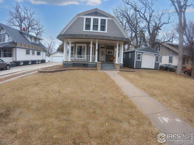 view of front of house featuring an outbuilding, covered porch, a gambrel roof, a front yard, and a garage