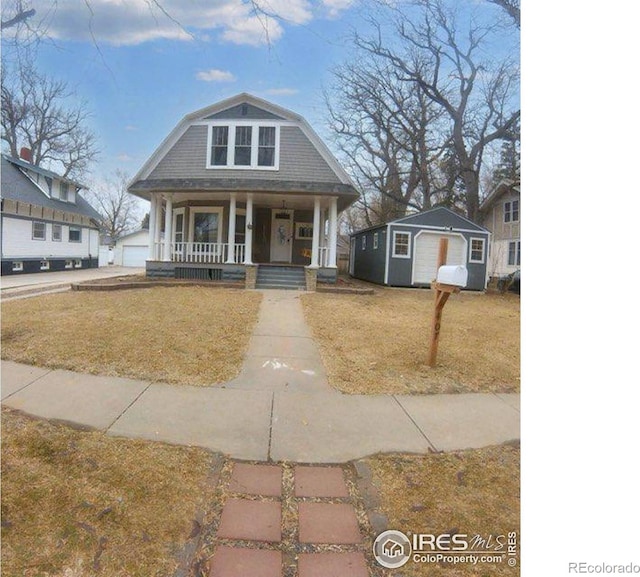 view of front of home with covered porch, a front lawn, a gambrel roof, and an outdoor structure