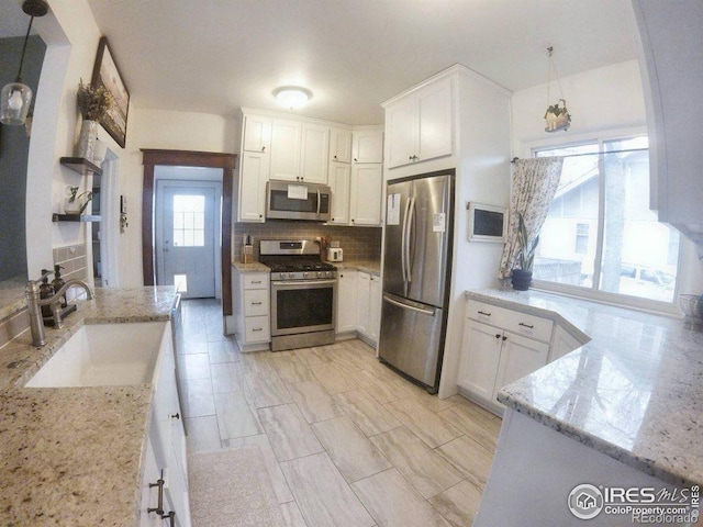 kitchen featuring backsplash, light stone counters, stainless steel appliances, and a sink