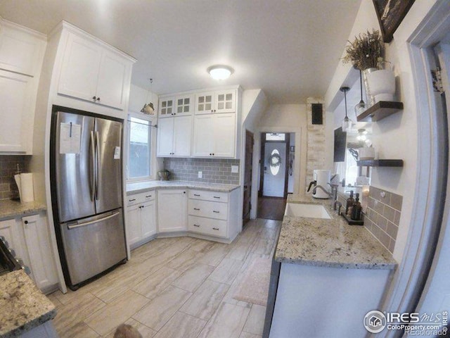 kitchen featuring tasteful backsplash, white cabinetry, a sink, and freestanding refrigerator