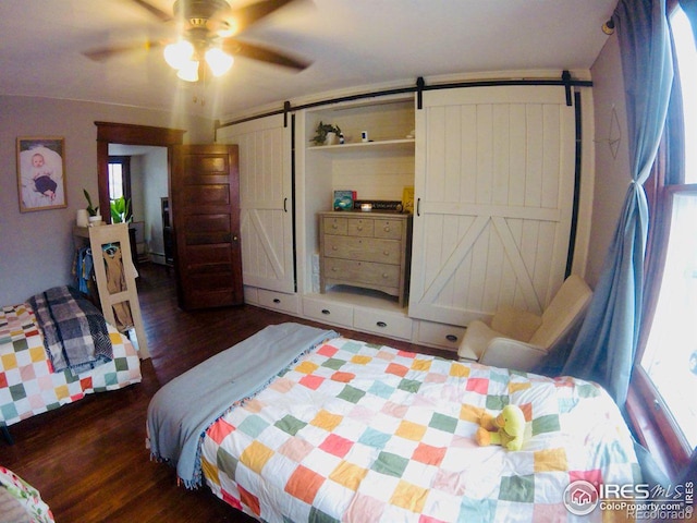 bedroom with a barn door, wood finished floors, and a ceiling fan