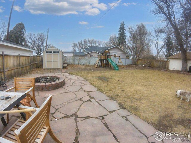 view of yard with a playground, a fenced backyard, a fire pit, an outdoor structure, and a storage unit