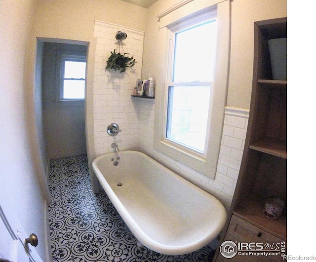 bathroom with tile walls, a freestanding bath, and tile patterned floors