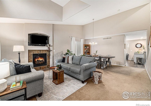 living room with visible vents, a tile fireplace, carpet floors, high vaulted ceiling, and a notable chandelier