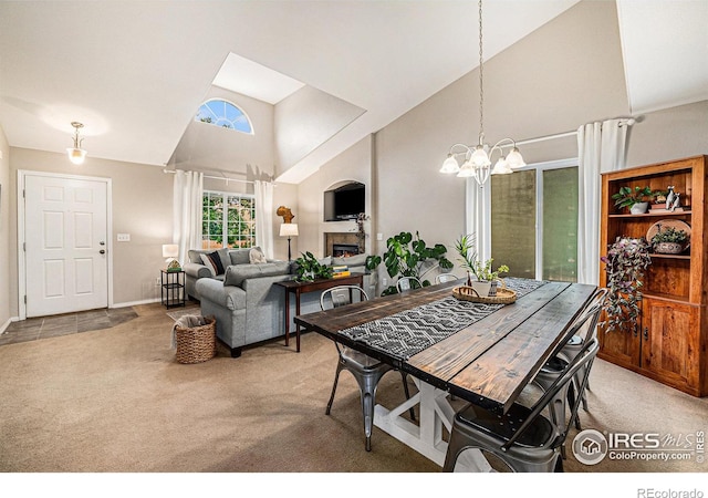 carpeted dining area with baseboards, a lit fireplace, high vaulted ceiling, and an inviting chandelier