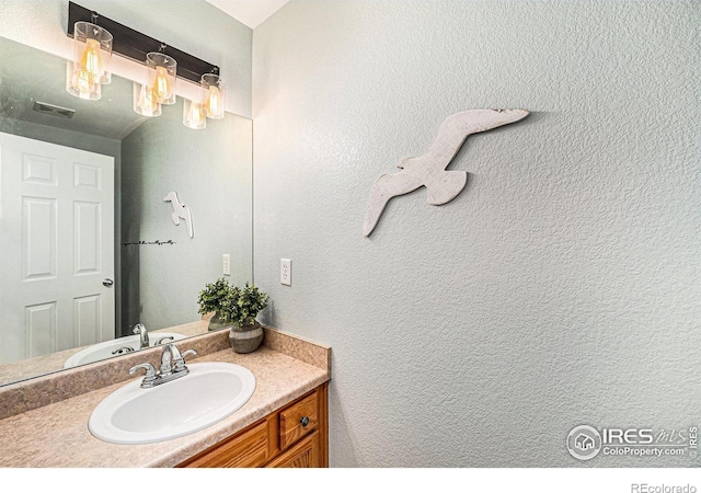 bathroom with a textured wall, visible vents, and vanity