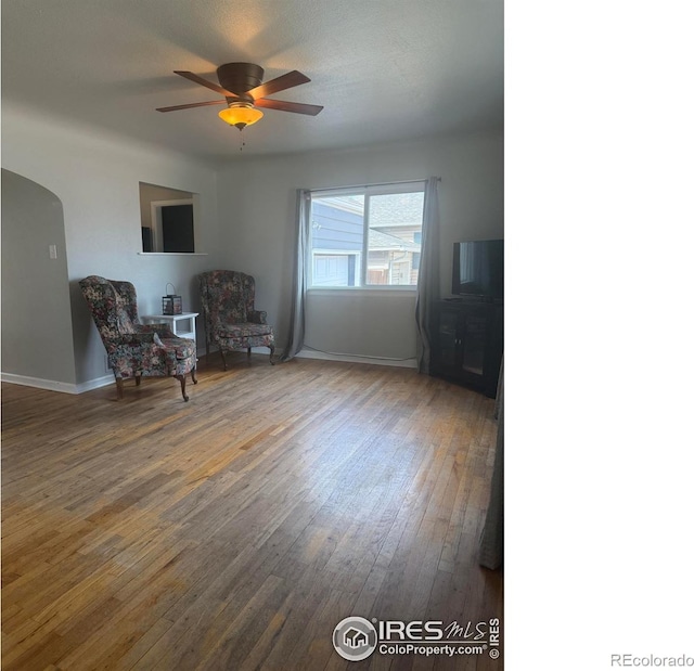 unfurnished room featuring arched walkways, baseboards, wood-type flooring, and ceiling fan