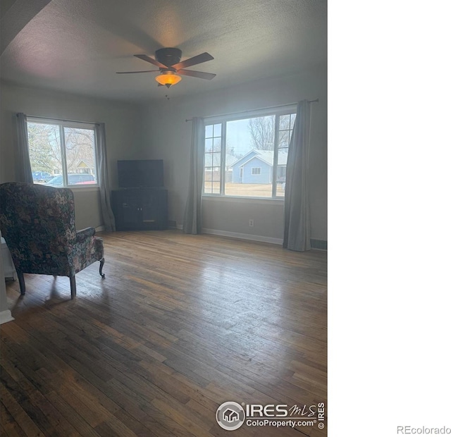 living area featuring a ceiling fan, wood finished floors, baseboards, and a textured ceiling