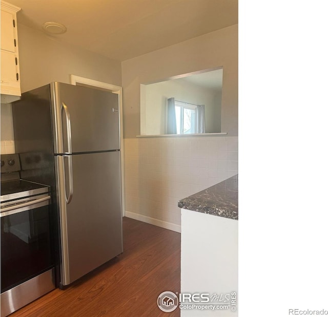 kitchen with dark wood-type flooring, stainless steel appliances, tile walls, white cabinets, and wainscoting