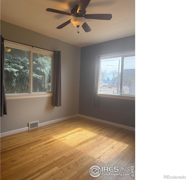 spare room with ceiling fan, wood finished floors, visible vents, and baseboards