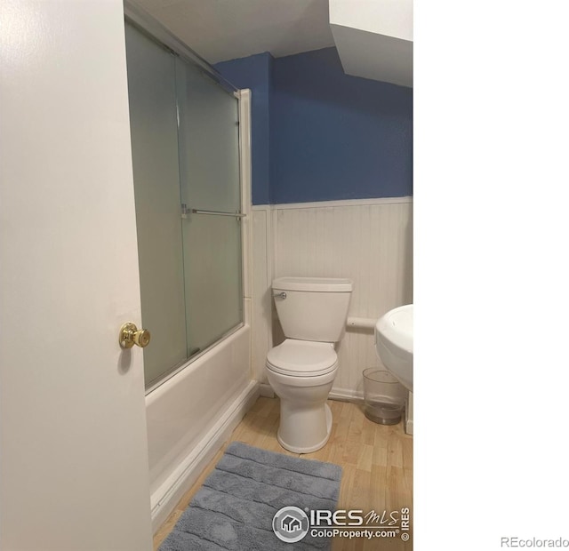 full bathroom featuring enclosed tub / shower combo, toilet, wood finished floors, and wainscoting