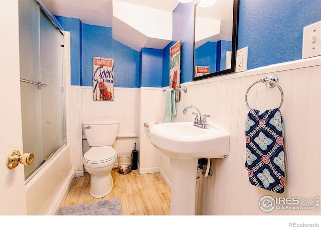 410 Cottonwood Ave, Eaton, CO 80615 - bathroom with wood finished floors, wainscoting, toilet, enclosed tub / shower combo, and a decorative wall