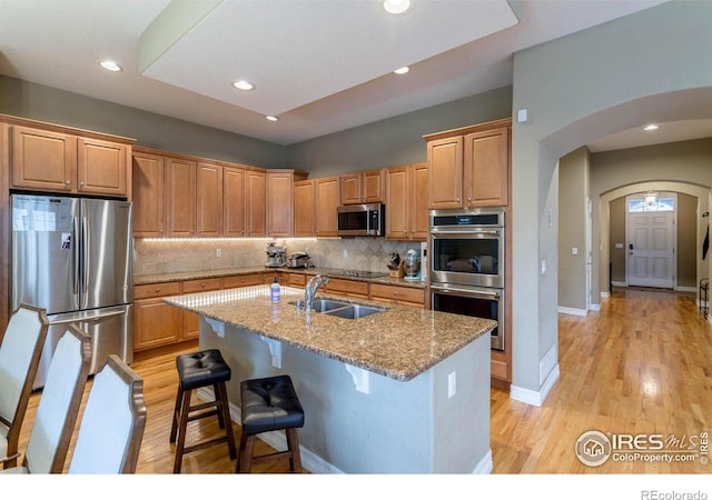 kitchen featuring arched walkways, appliances with stainless steel finishes, light wood-type flooring, and a sink