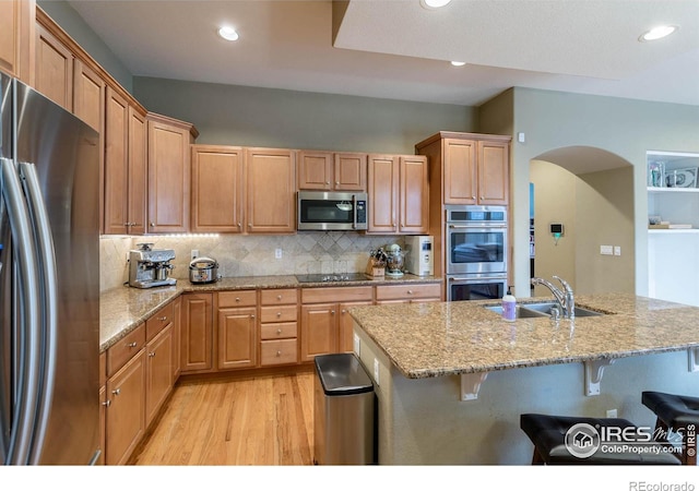 kitchen featuring arched walkways, stainless steel appliances, a sink, a kitchen breakfast bar, and tasteful backsplash