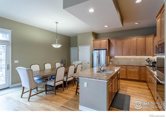 kitchen featuring stone counters, a sink, freestanding refrigerator, decorative backsplash, and a center island with sink