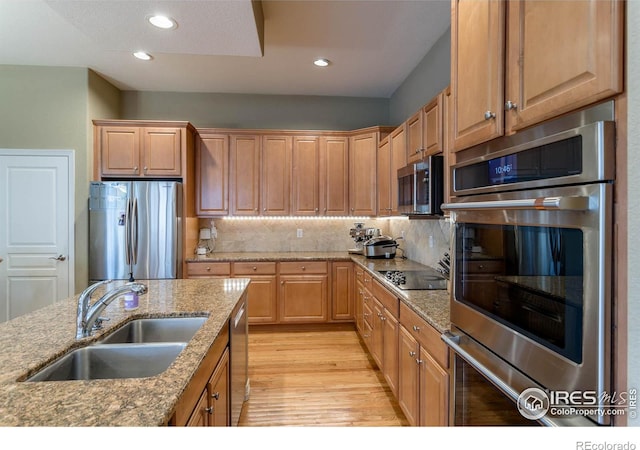 kitchen featuring light wood-style flooring, a sink, appliances with stainless steel finishes, decorative backsplash, and light stone countertops