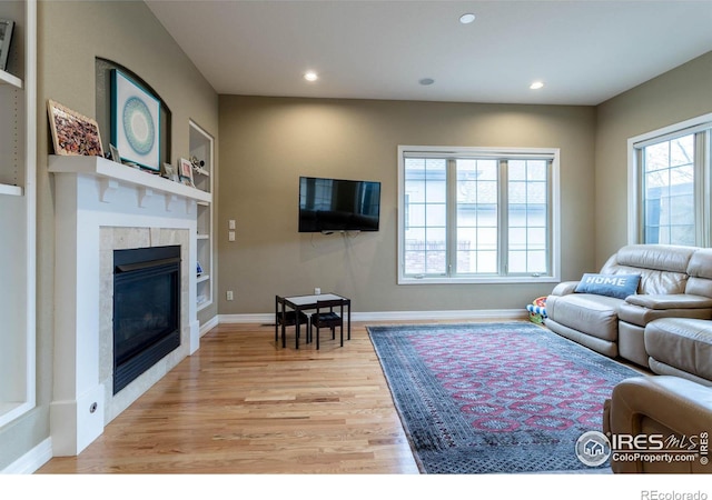 living room with recessed lighting, a fireplace, baseboards, light wood-style floors, and built in features