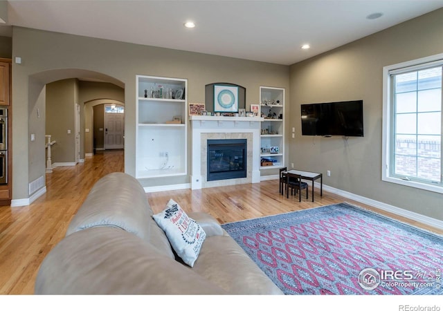 living room with light wood-style floors, baseboards, built in features, and a tile fireplace