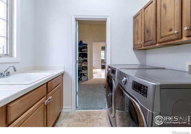 clothes washing area with separate washer and dryer, a sink, and cabinet space