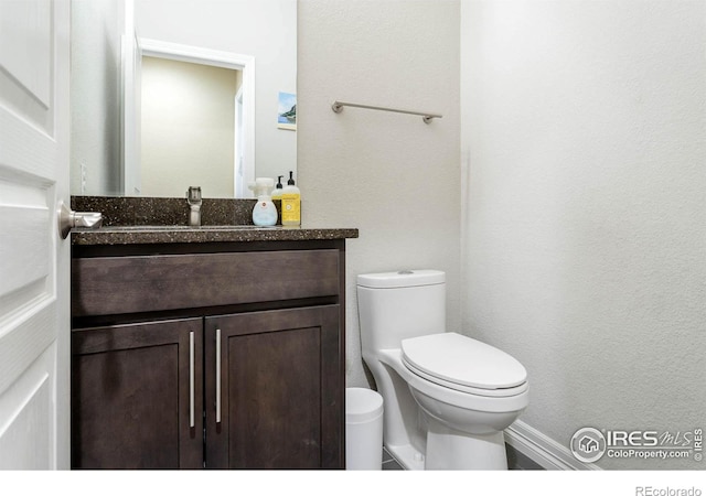 half bath with a textured wall, vanity, and toilet