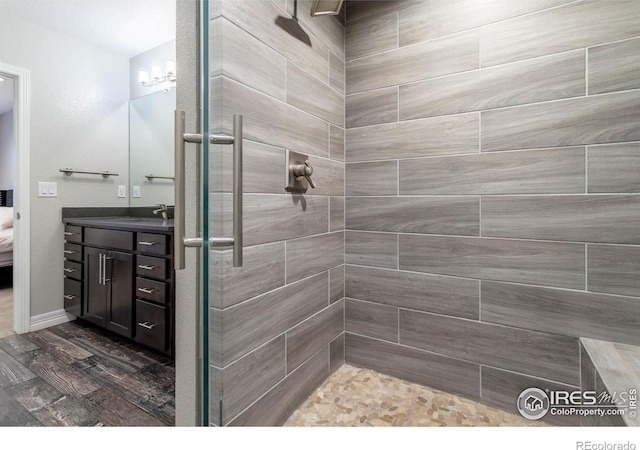 ensuite bathroom with baseboards, tiled shower, ensuite bath, wood finished floors, and vanity