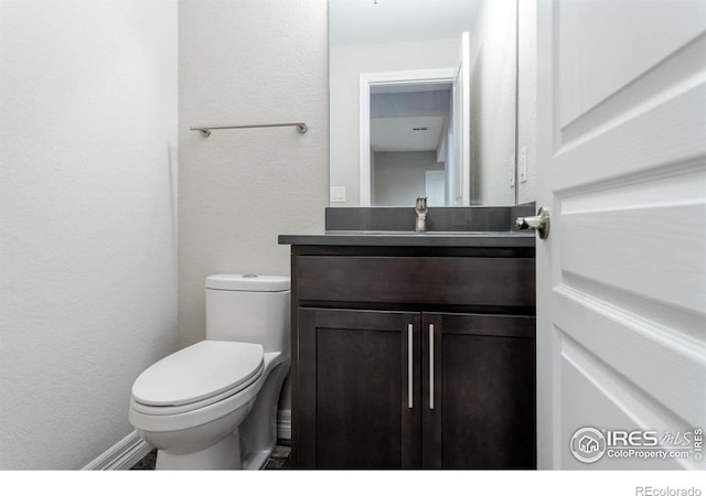 bathroom featuring toilet, a textured wall, and vanity