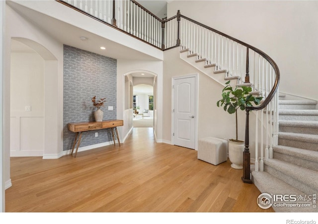 foyer entrance featuring wood finished floors, arched walkways, a high ceiling, baseboards, and stairs