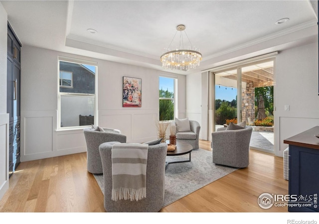 living room featuring a decorative wall, a wainscoted wall, light wood-type flooring, ornamental molding, and a notable chandelier