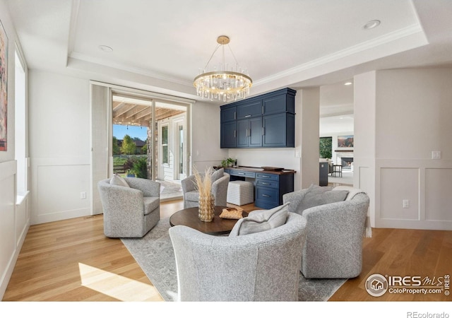 living room with a tray ceiling, a decorative wall, a fireplace, light wood finished floors, and a chandelier