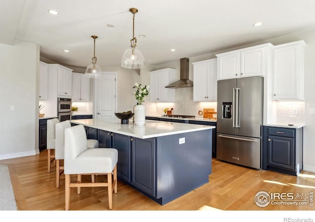 kitchen featuring wall chimney exhaust hood, a kitchen island, light wood finished floors, and stainless steel appliances