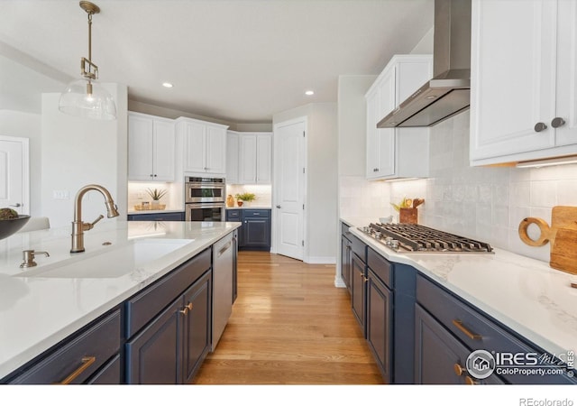 kitchen with light wood-style flooring, a sink, stainless steel appliances, white cabinets, and wall chimney range hood