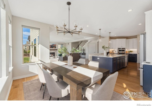 dining room with recessed lighting, a fireplace, stairs, light wood-style floors, and a notable chandelier