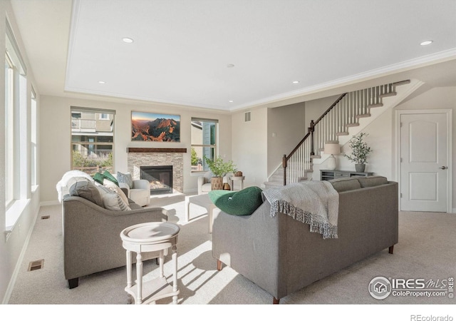 living area featuring a wealth of natural light, a stone fireplace, carpet flooring, and stairs