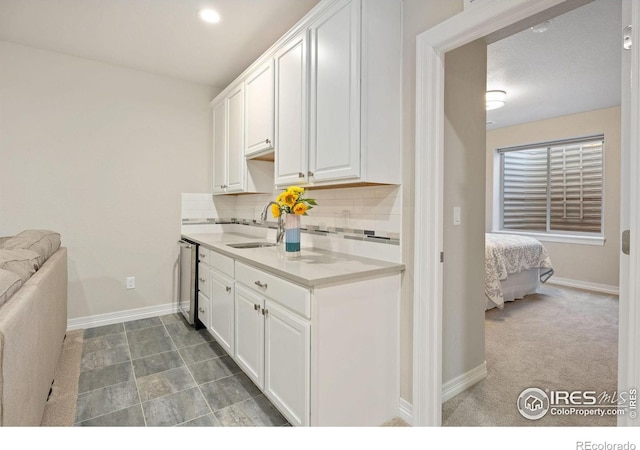 kitchen featuring backsplash, baseboards, light countertops, white cabinets, and a sink