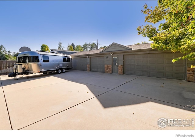 ranch-style house featuring a garage, concrete driveway, stone siding, and fence