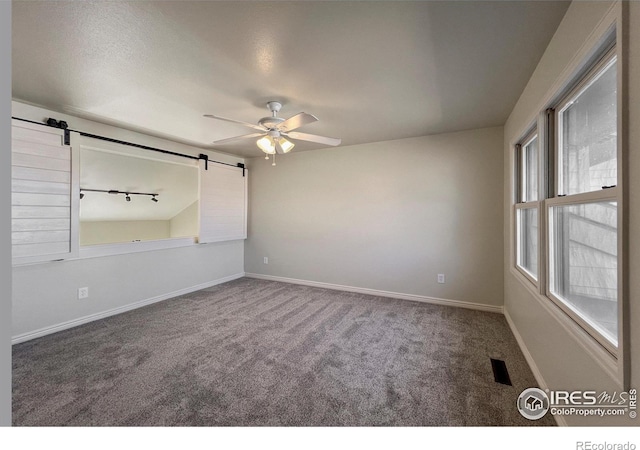 unfurnished room featuring a barn door, carpet floors, visible vents, a ceiling fan, and baseboards