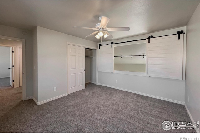 unfurnished bedroom with a barn door, a closet, baseboards, and carpet flooring