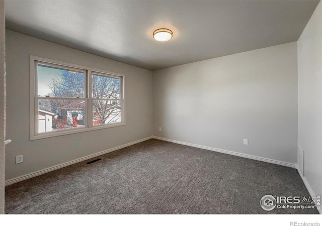 spare room featuring dark carpet and baseboards