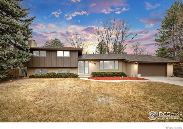 split level home featuring a front yard, concrete driveway, a chimney, and an attached garage